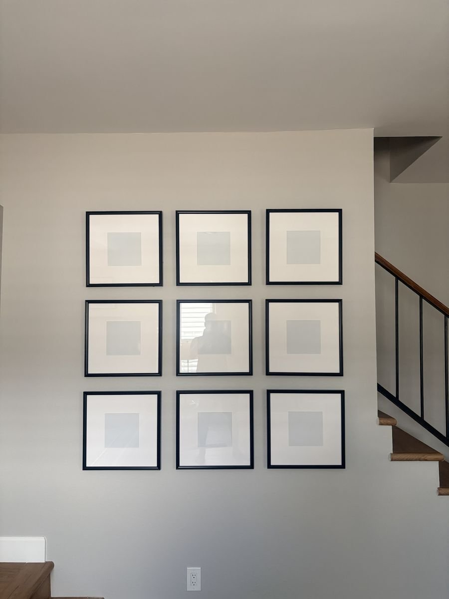 Nine black frames hung in an even 3x3 grid gallery wall beside a staircase
